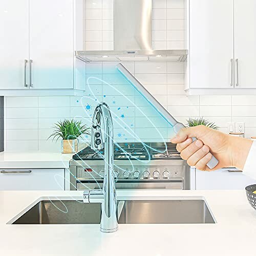 Hand using UV light sanitizer in modern kitchen with stainless steel appliances.