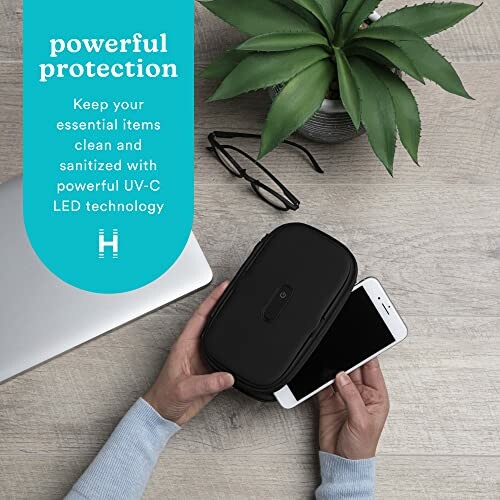 Person holding phone over UV-C sanitizer next to laptop and glasses.